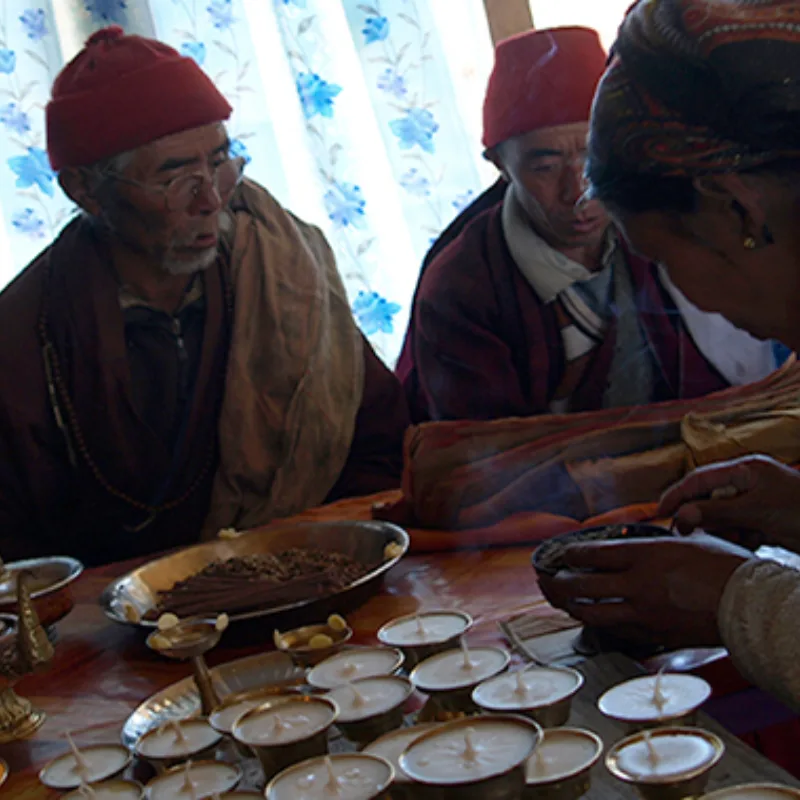 Buddhist monks in red robes lighting traditional brass butter lamps and incense during a spiritual ritual in Nepal.