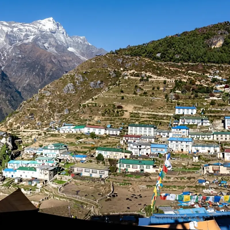 Traditional stone Sherpa village stepped on a hillside beneath a soaring snow-capped mountain in Nepal.