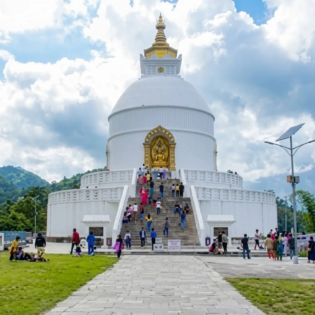 White dome of the World Peace Pagoda with golden Buddha niche and visitors on stone stairs in Pokhara.
