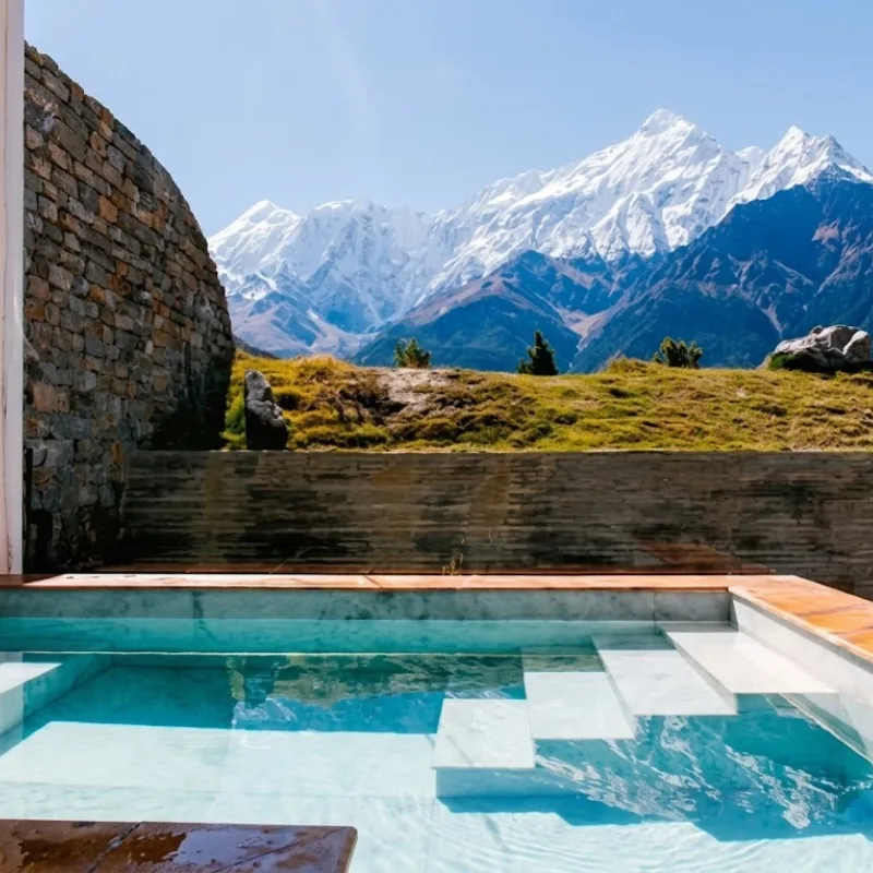Luxury infinity pool terrace facing a towering snow-covered Himalayan mountain massif under blue skies.