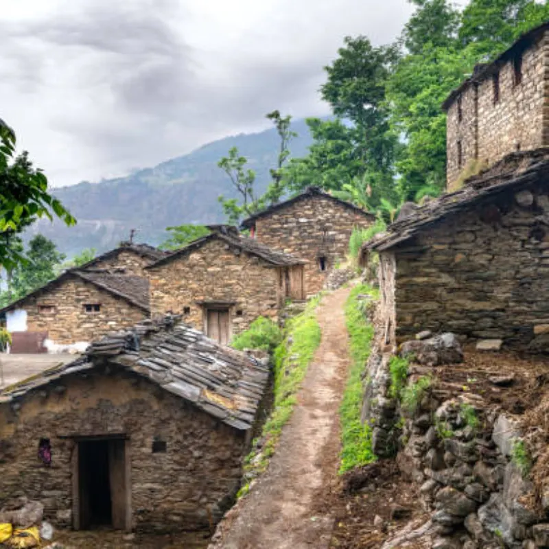 Narrow dirt footpath winding between rustic stone masonry houses in a hillside mountain village in Nepal.