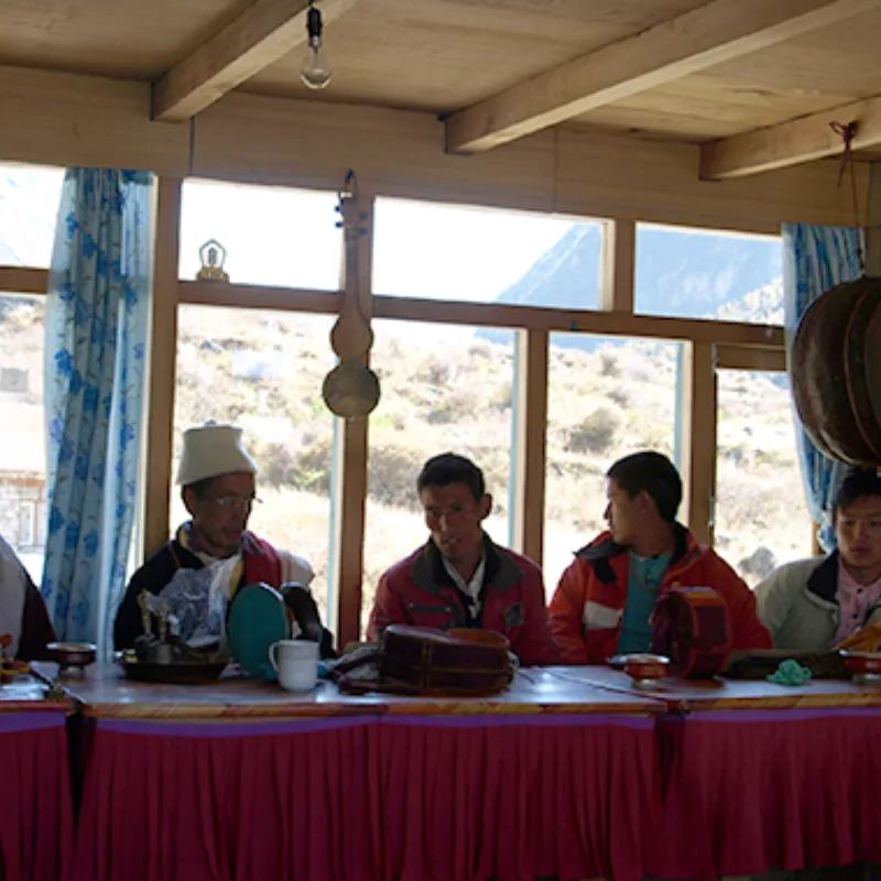 Tibetan Buddhist monks and local Himalayan men seated behind a ceremonial table during a traditional gathering.