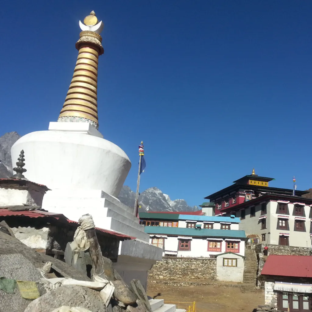 White Tibetan Buddhist chorten with a golden spire standing in the courtyard of Tengboche Monastery under a deep blue sky.