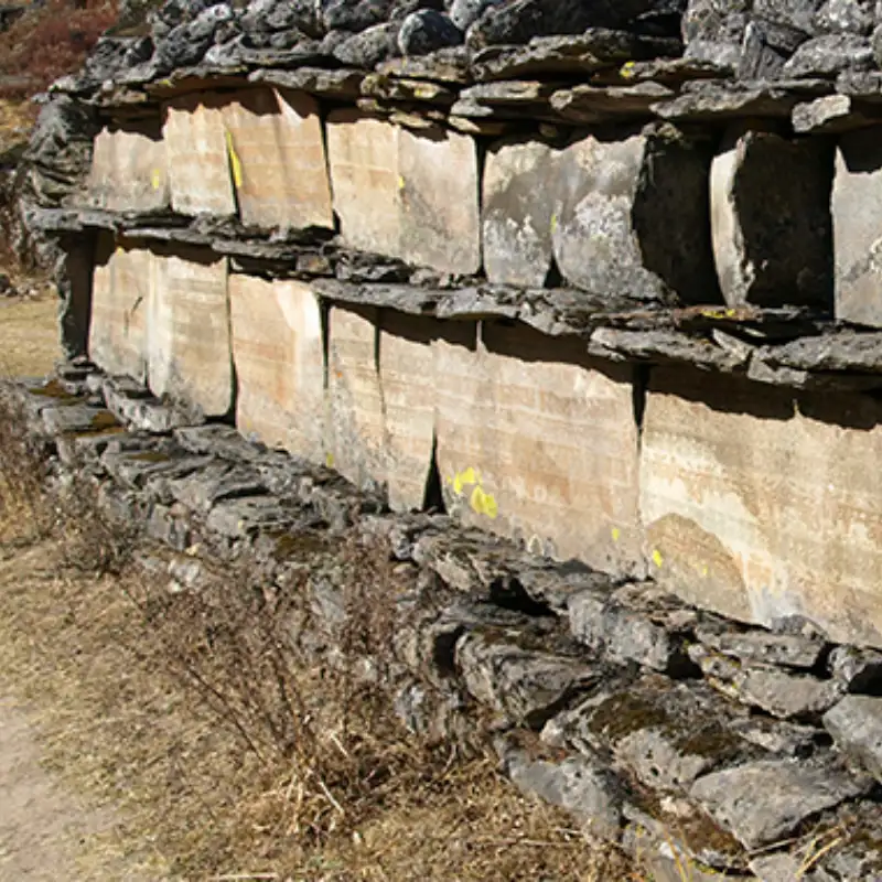 Ancient Buddhist Mani stone wall inscribed with sacred Tibetan mantras along a mountain trekking trail.