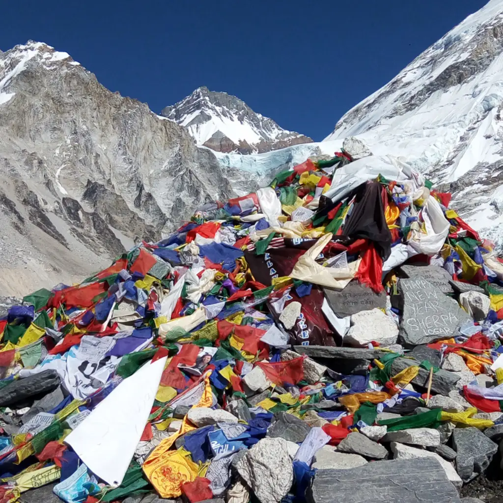 Large sacred stone cairn draped in colorful Buddhist prayer flags at Everest Base Camp, with Mount Nuptse and Khumbu Glacier peaks in the background.