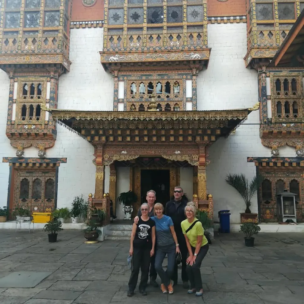 Group of tourists posing in the courtyard of a traditional Bhutanese building with ornate wooden architecture.